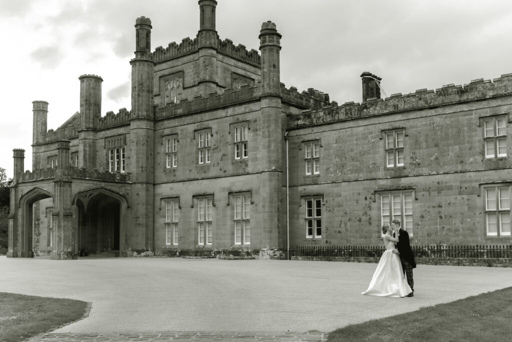 Couple kiss in front of Blairquhan Castle on their private estate sailcloth marquee wedding day in Scotland.