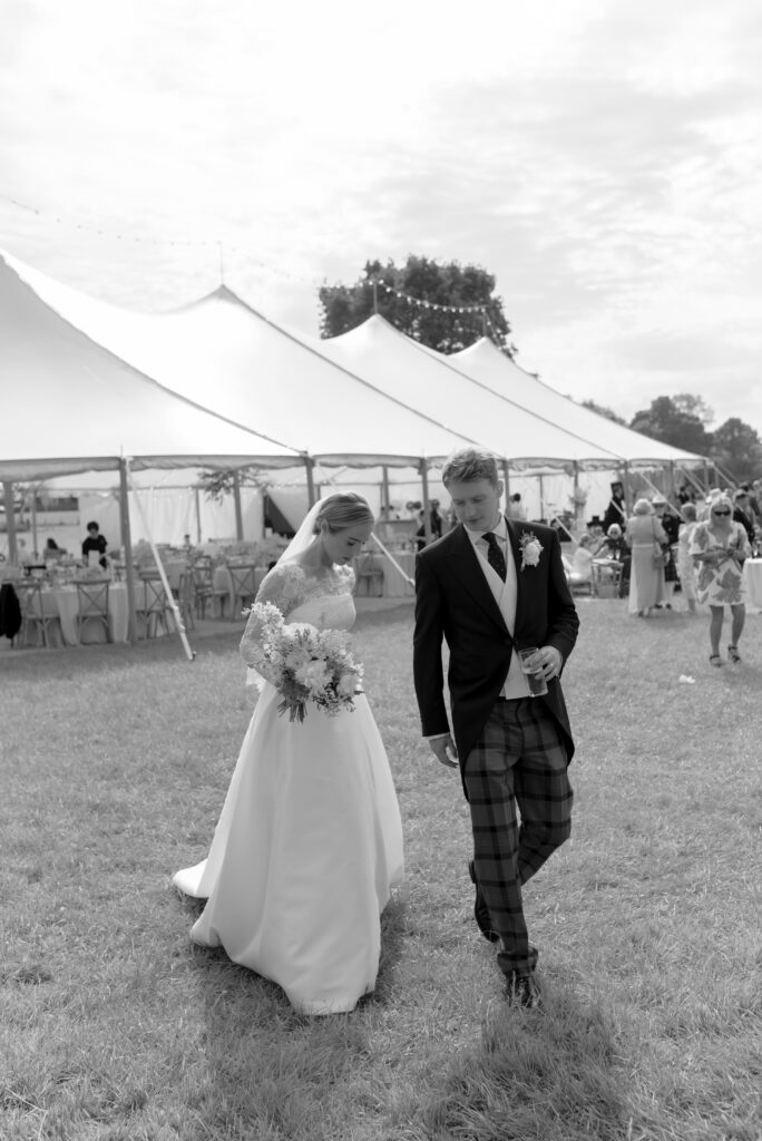 Bride and groom walking from sailcloth marquee wedding reception in private castle estate wedding Scotland with guests in the background