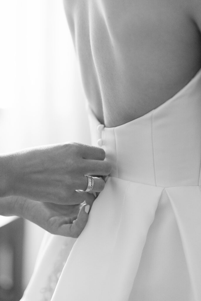 Close-up of bride fastening wedding dress with clean, minimalist satin fabric and soft natural light