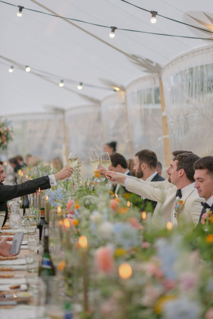 Guests toast speeches in sailcloth marquee on Penicuik Estate, Scotland destination wedding venue. Image by Penicuik House recommended wedding photographer, Jill Cherry Porter.