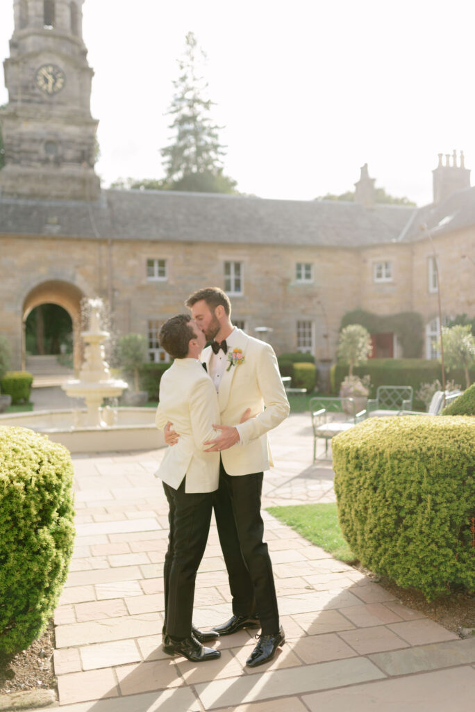 Grooms kiss in the courtyard as sun sets over Penicuik House, Scotland destination wedding venue on their wedding day. Image by Penicuik Estate recommended wedding photographer, Jill Cherry Porter.